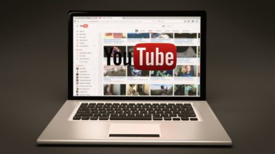 Bild på en uppfälld bärbar dator som står på ett bord. Youtubes förstasida syns.